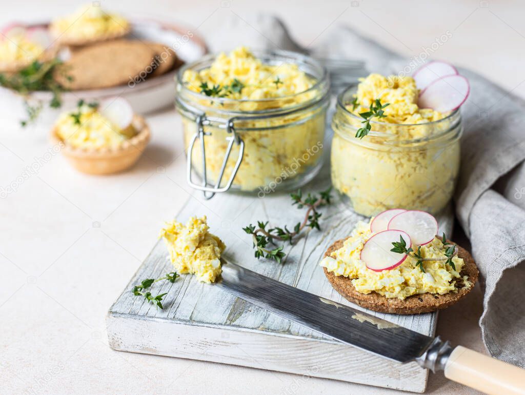 Tartlets with egg pate or salad and radish and thyme on light stone background. Egg dip in glass jar.