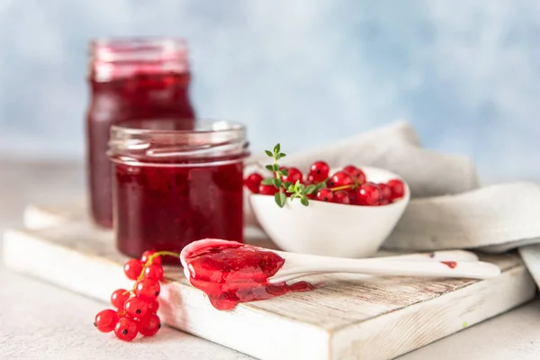 Mermelada casera de grosella roja o gelatina en frascos de vidrio y grosellas rojas bayas frescas en tabla de cortar de madera. — Foto de Stock