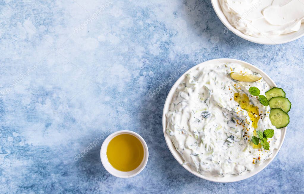 Indian or Pakistani raita sauce or dip with cucumber, yoghurt, garlic and mint, blue concrete background. Traditional Indian cuisine. Selective focus. Top view.