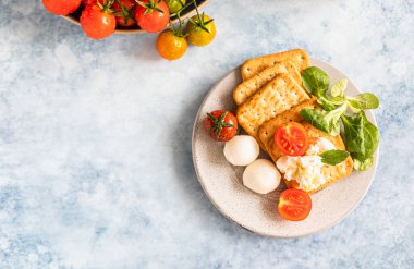 Kiraz domatesli krakerler, yeşil salata ve mozzarella, mavi beton arka plan. Üst görünüm.