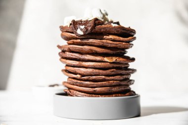 Bir yığın ev yapımı çikolatalı krep, erimiş çikolata, badem ezmesi ve lokum, hafif arka plan. Doğrudan güneş ışığı ve sert gölgeler.