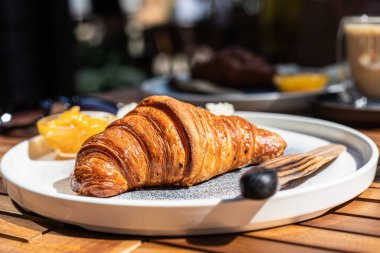 Kahvaltıda kruvasan ve bir fincan cappuccino, sabahın erken saatlerinde bir sokak kafesinde masanın üstünde. Seçici odak.