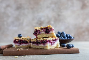 Yabanmersini dolgulu, taze yaban mersinli ve betondan arkaplanlı peynirli kek barları. Peynirli kek, yaban mersini ve streusel ile dilimler. Seçici odak.