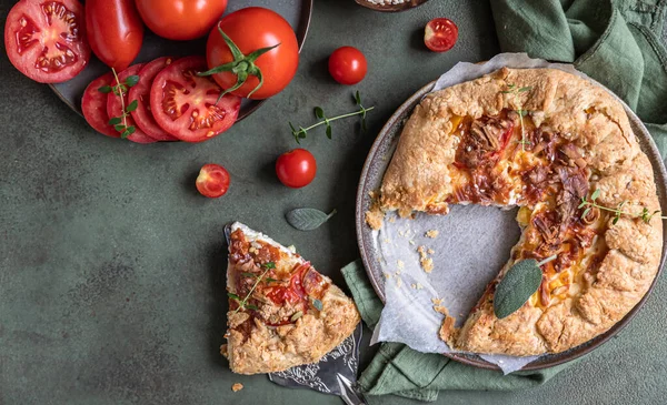 Вкусный томатный пирог, открытый пирог или галет с помидорами и сыром, украшенный ароматическими травами на зеленом бетонном фоне. — стоковое фото