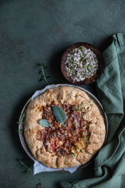 Baharatlı domates turtası, açık turta ya da yeşil beton arka planda aromalı otlarla süslenmiş domates ve peynirli galette. Üst görünüm.