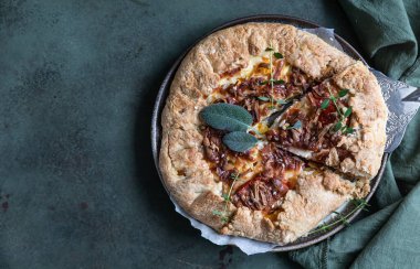 Baharatlı domates turtası, açık turta ya da yeşil beton arka planda aromalı otlarla süslenmiş domates ve peynirli galette. Üst görünüm.