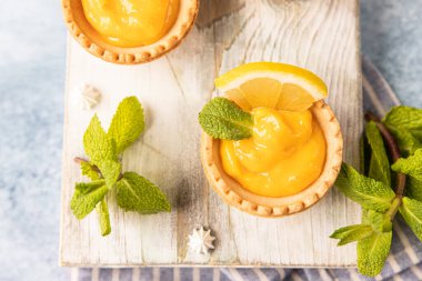 Limon kaymağı, nane ve limon dilimleri ve ahşap tahtada mini kremalı turta, mavi beton arka plan. Üst görünüm.