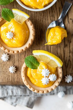 Limonlu turta. Ev yapımı, limonlu mini tartlar ve ahşap tahtada krema, açık beton arka plan. Üst görünüm.