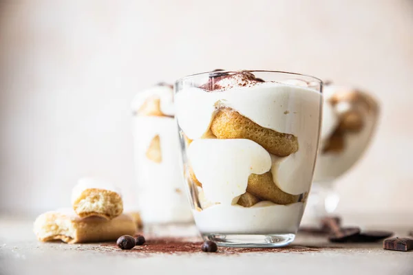 Tradizionale dolce italiano tiramisù in vetro, fondo pietra chiara. Dessert di porzione aromatizzato al caffè a base di ladyfingers e mascarpone decorato con cacao. — Foto Stock