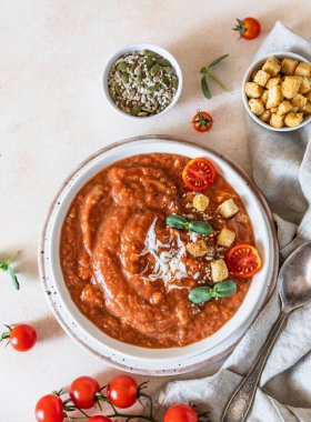 Pişmiş domatesli sebze çorbası, dolmalık biber, krema, ekmek kırıntıları ve açık beton arka planda beyaz kasede mikro yeşiller. Seçici odaklanma. Üst görünüm.