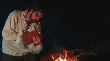 Dışarıda ateşin yanında okuyan şair.