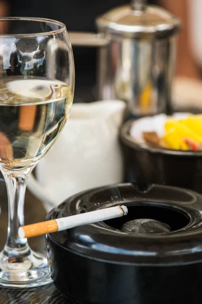 Glas Weißwein mit Aschenbecher und Zigarette auf dem Tisch — Stockfoto