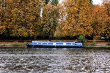 Geleneksel nehir yüzen ev teknesi Nehir kıyısına demirlemiş Arka planda altın sonbahar ağaçlarıyla
