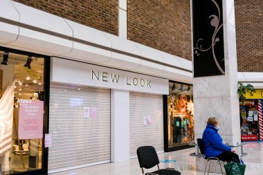 Londra İngiltere, 26 Kasım 2020, COVID-19 Kilitleme sırasında New Look Moda Perakendecisi 'nin kapalı bir şubesinin önünde oturan yalnız bir kadın.