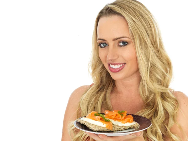 Mujer joven comiendo salmón ahumado y queso crema en una galleta — Foto de Stock