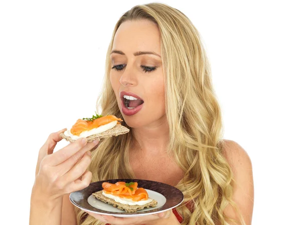 Jovem mulher comendo salmão defumado e queijo creme em um biscoito — Fotografia de Stock