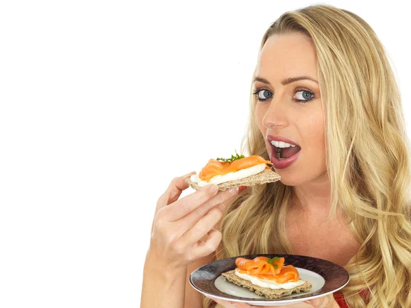 Mujer joven comiendo salmón ahumado y queso crema en una galleta —  Fotos de Stock