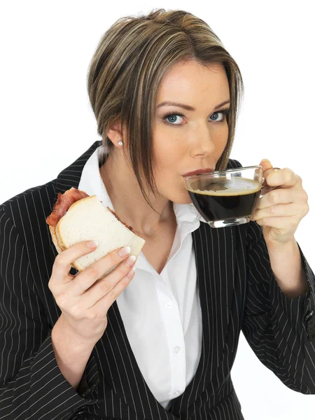 Joven mujer de negocios comiendo un sándwich de tocino y café negro — Foto de Stock