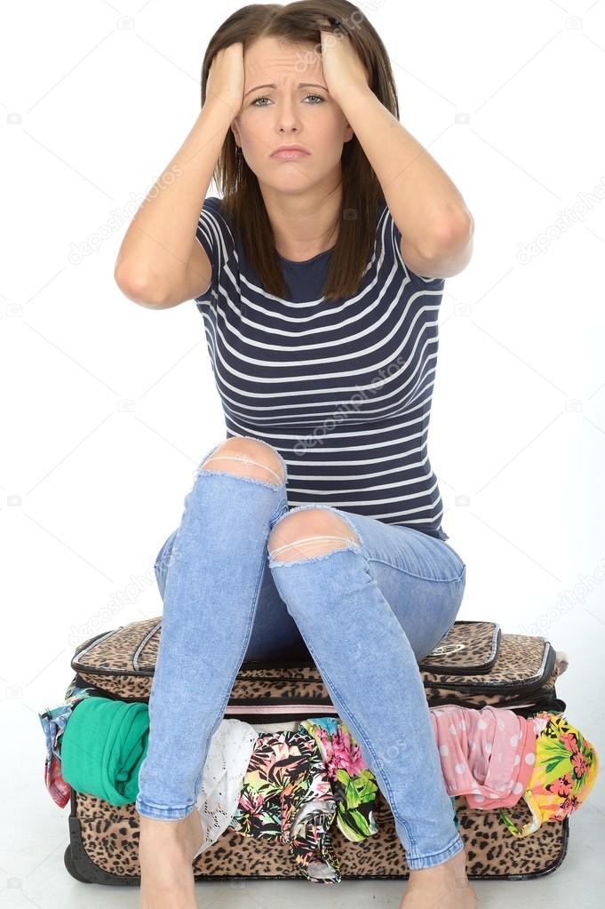 Frustrated Attractive Young Woman Trying To Close a Packed Suitcase By Sitting on it