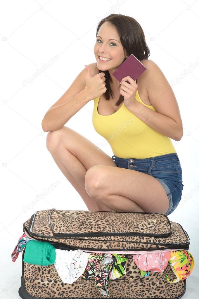Happy Please Young Woman Kneeling on a Packed Suitcase Holding a Passport Travel Document