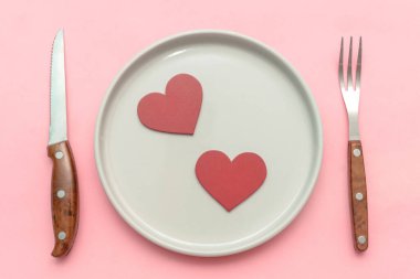 Sevgililer Günü yemek randevusu konsepti. Masa servisi, pembe arka planda çatal bıçak takımı. Üst görünüm düzlüğü.