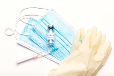 Coronavirus aşısı şişesi, Covid-19 'a karşı koruma, sağlık şırıngası, tıbbi maske ve eldivenler, düz yatak. Aşı enjeksiyonuyla önleme hastalığı