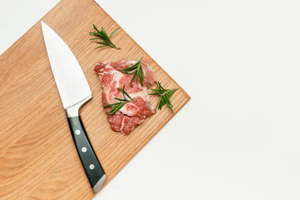 raw fresh beef meat steak with rosemary and knife on cutting board isolated on white background, copy space, food cooking at home, top view.