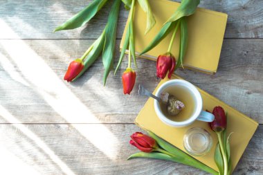 Bir fincan çay, bir buket kırmızı lale, çiçekler ve kitaplar. Kadınların anneler günü konsepti fotokopi alanı ile.