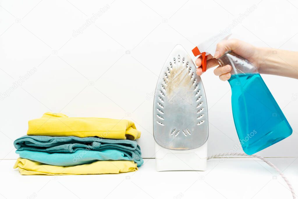 laundry pile of colorful clothing, stack of clothes isolated on white background. woman cleaning dirty rusty iron with cleaning agent in a bottle.