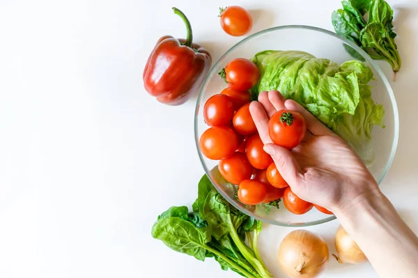 女性の手は コピースペースのある白いテーブルの背景に有機野菜やバイオ新鮮な野菜のボウルにトマトを保持します 健康的な自然な熟した菜食主義の野菜の概念 サラダの材料 — ストック写真