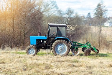 Mavi, küçük, modern traktör makineleri güneşli bir günde çiftlikte tarla sürerler. Çiftçi bitki ve ekin ekmeden önce toprak ekip biçiyor ve ekiyor, kırsal doğa manzarası..