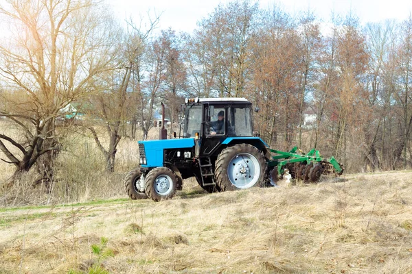 晴れた日に農場で農地の牧草地を耕す青い小さな近代的なトラクター機械 植物や作物 自然の田園風景を播種する前に 農家の栽培と土壌の耕作を行う — ストック写真