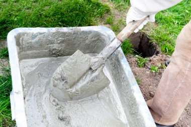 Eldivenleri karıştıran, çimento çamuru karıştıran, beton harcı büyük kasede kürekle karıştıran işçi elleri, su deposu, yalak, kova. İnşaat süreci, yenileme, temel atma hazırlıkları.