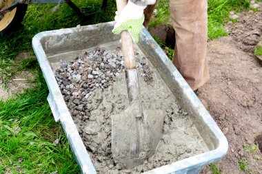 İşçi elleri eldiven karıştırıyor, çimento çamuru karıştırıyor, beton moloz harcı ile büyük kasede kürek, su deposu, yalak, kova. İnşaat süreci, yenileme, temel atma hazırlıkları