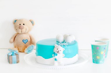 Karton bardaklarla süslenmiş bebek mavisi pasta, hediye kutusu ve ilk doğum günü kutlaması için oyuncak ayı. Bebek partisi için mavi renkli süslemeler..