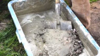 İşçi karıştırıyor, karıştırıyor, çimento karıştırıyor, beton moloz molozuyla büyük kâsede kürek, su deposu, yalak, kova. İnşaat süreci, yenileme, temel atma hazırlıkları.