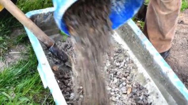 İşçi karıştırıyor, karıştırıyor, çimento karıştırıyor, beton moloz molozuyla büyük kâsede kürek, su deposu, yalak, kova. İnşaat süreci, yenileme, temel atma hazırlıkları.