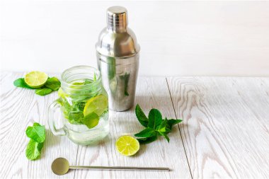 Taze buzlu mojito limonata yaz içeceği dilimlenmiş limonlu kokteyl, parlak yeşil nane yaprakları şeffaf bir fincanda titretici ve donmuş buz küpleri ahşap masada taş kavanozu..