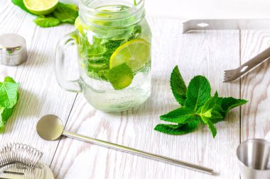 Taze buzlu mojito limonata yaz içeceği dilimlenmiş kireç, parlak yeşil nane yaprakları ve şeffaf bir fincanda donmuş buz küpleri ahşap masada taş kavanozu..