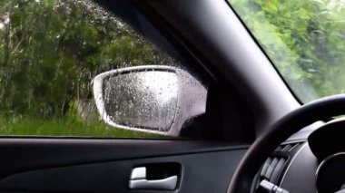 Aynanın içinde yağmur damlaları araba camına düşüyor. Ağaçlar bulanık. Yaz günü arka plan bulanık..