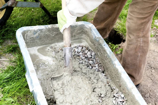 Arbetare blandar, rör om cement flytgödsel, betong grus murbruk med spade i stor skål, reservoar, tråg, hink. Förberedelse för byggprocess, renovering, grundläggning — Stockfoto