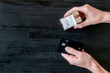 Elinde altın yüzük ve kredi kartı olan hediye kutusu olan kadın elleri siyah ahşap masada. satın alma hediyesi, mücevher, finans, para, bankacılık konsepti, üst görünüm, kopyalama alanı