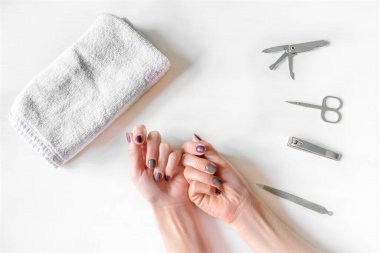 Tırnakları cilalanmış ve manikür aletleri takmış kadın elleri. Beyaz kadın evde ya da manikürcüde Fransız manikürü yaptırıyor. Manikür, kişisel bakım, güzellik prosedürleri.