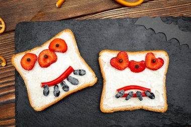 Cadılar bayramında kızarmış ekmek, tereyağı, çilek, şeker, servis masası, siyah arka planda yarasalar. Çocuklar için tatlı öğle yemeği..