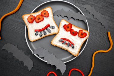 Cadılar bayramında komik canavar suratı tereyağlı tost ekmeği, tatlılar, siyah arka planda yarasalar. Çocuklar için tatlı tatlı öğle yemeği.