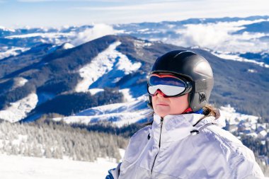 Kış tulumu giymiş, kar maskesi takmış, kar tepesinde, yüksek dağlarda Alp disiplini kayak merkezi, doğa manzarası olan tecrübeli olgun bir kadın..
