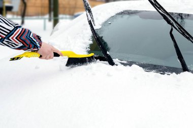 Adam arabanın ön camından fırçayla kar ve buz fırçalıyor. Kışın arabadan kar fırtınası üstüne taze kar temizleyen kişi.
