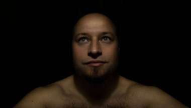 Sakallı bir adam karanlıkta yukarı bakıyor.