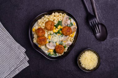 Sebzeli makarna ve siyah arka planda beyaz soslu köfte. Seçici odak.