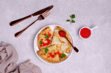 Hafif çimento arka planında kırmızı balık yumurtası ve seramik tabakta kızarmış krep. Seçici odak.